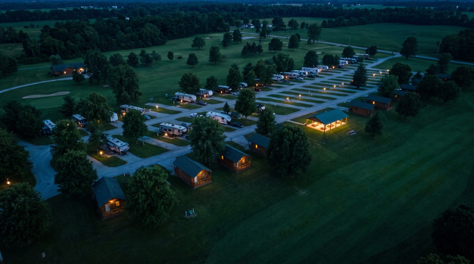 Illustrative image, not the actual property. RV sites with lit hookup posts, small cabins and an event pavilion on open rolling land at dusk