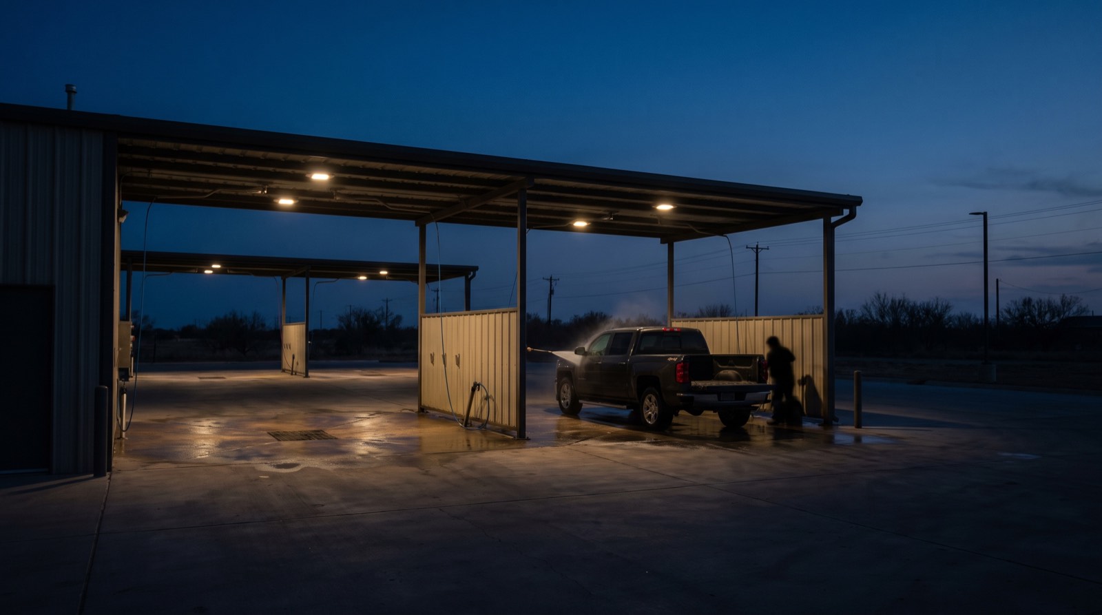 Illustrative image, not the actual property. Lit self-service car wash bays at dusk with a pickup truck being washed